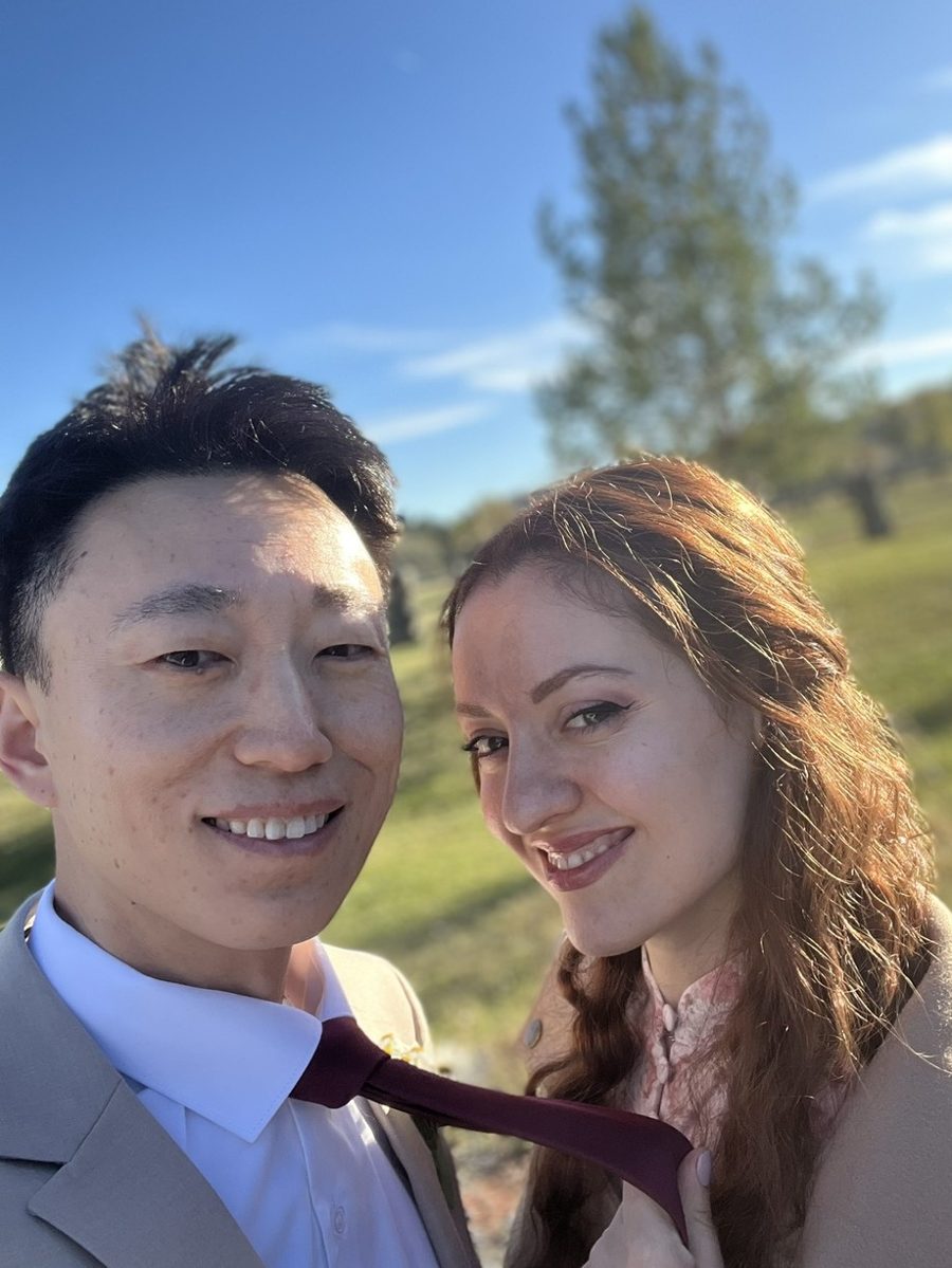 Aaron and Liuba Xu outdoors on a sunny day, she is tugging his tie