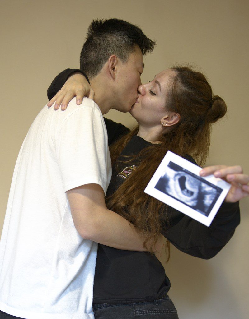 Aaron and Liuba Xu kissing while she holds up their first ultrasound